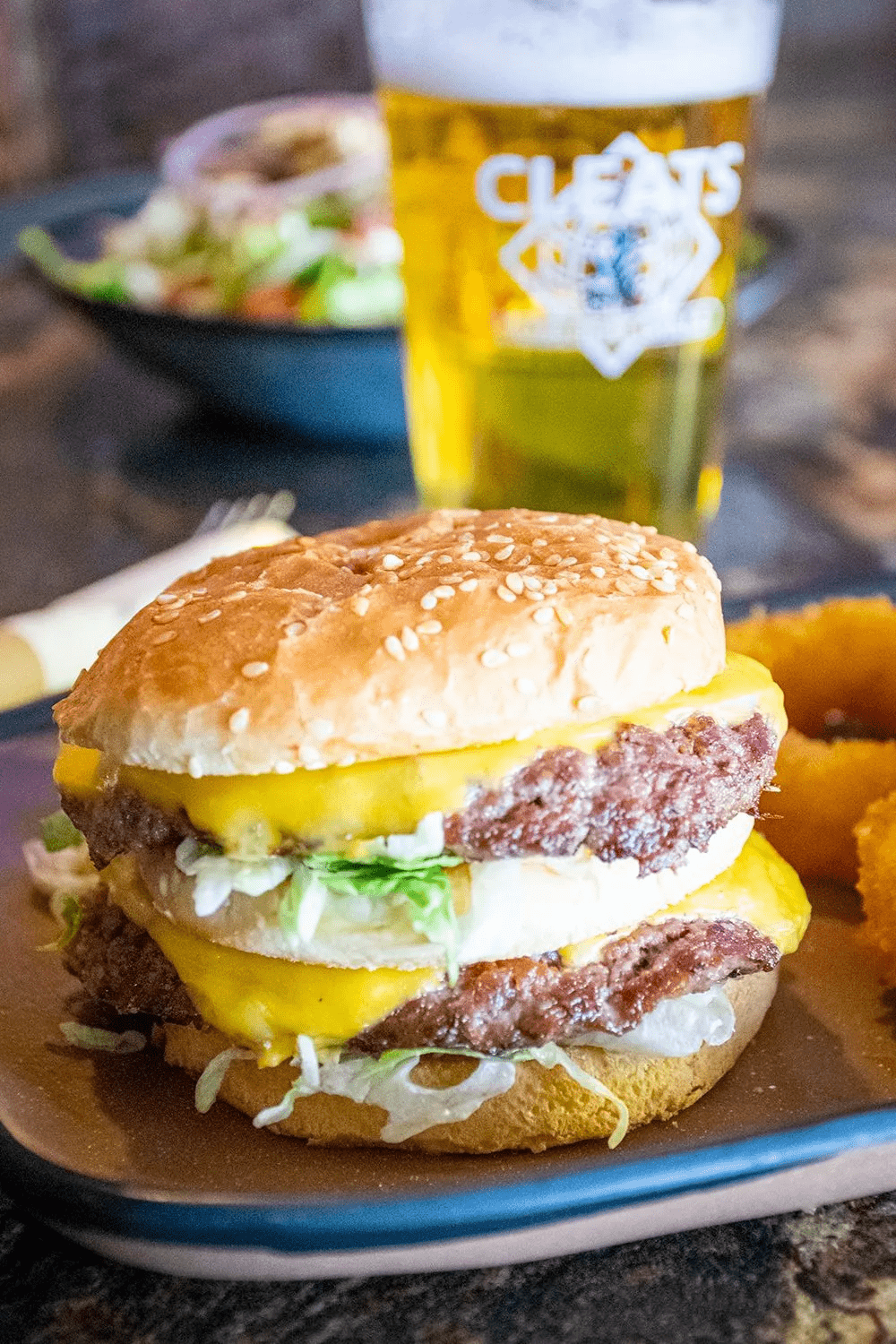 Double-decker cheeseburger with beer, salad, and onion rings on a plate.