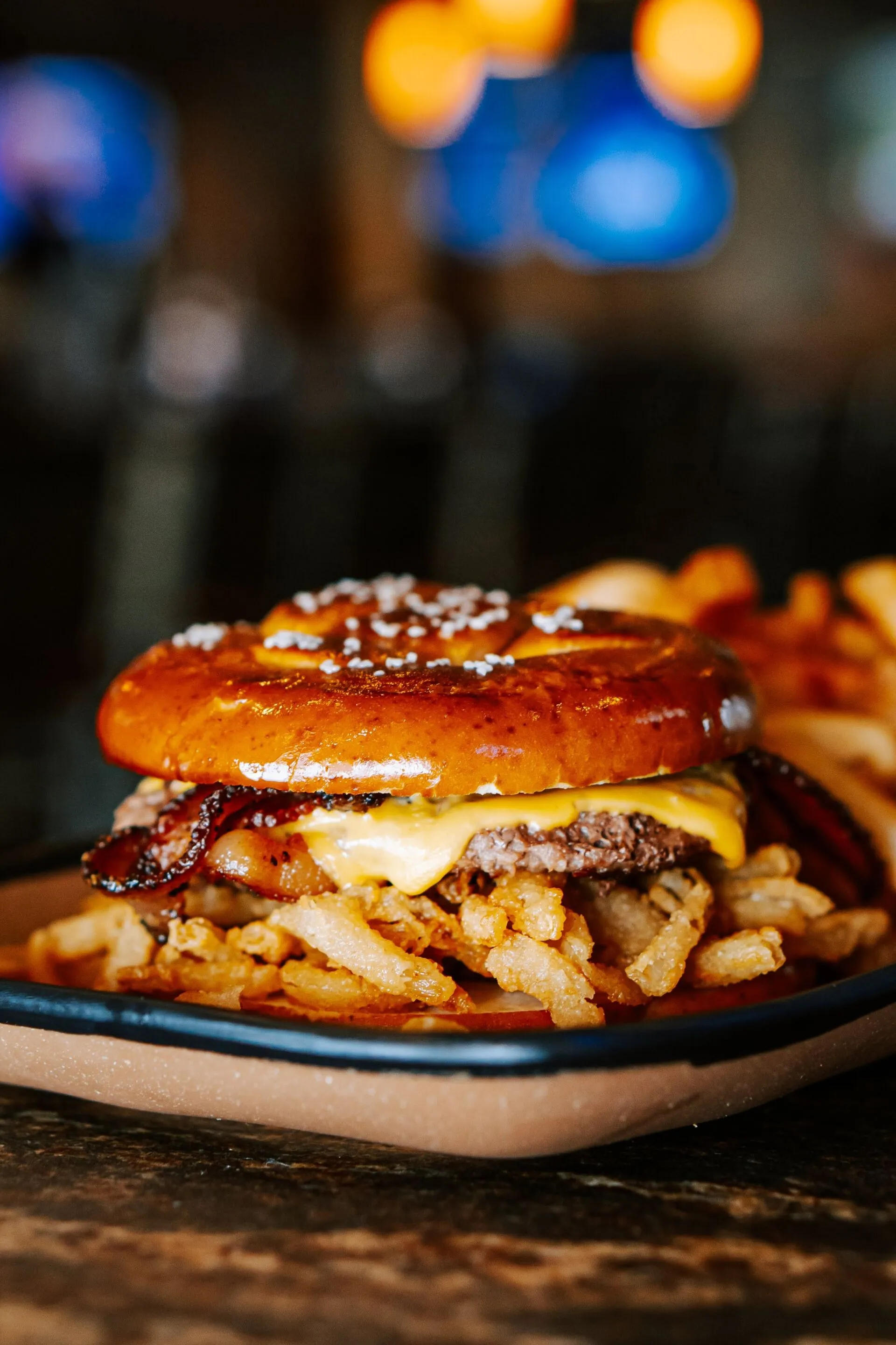 Burger with fries on a plate. Pretzel bun, cheese, bacon, and fried onions.