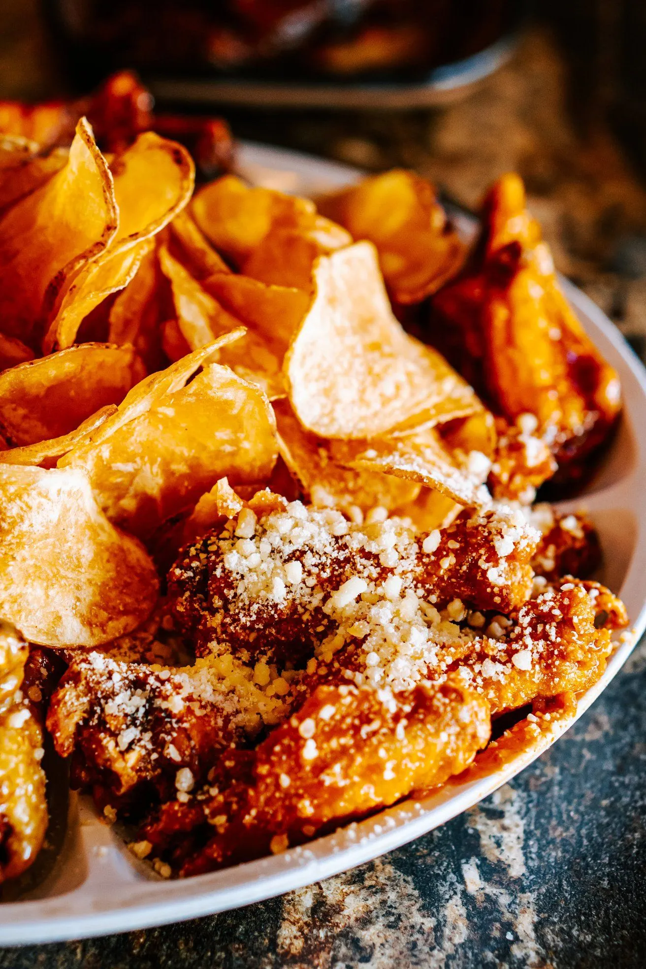 Chicken wings and potato chips topped with parmesan cheese.