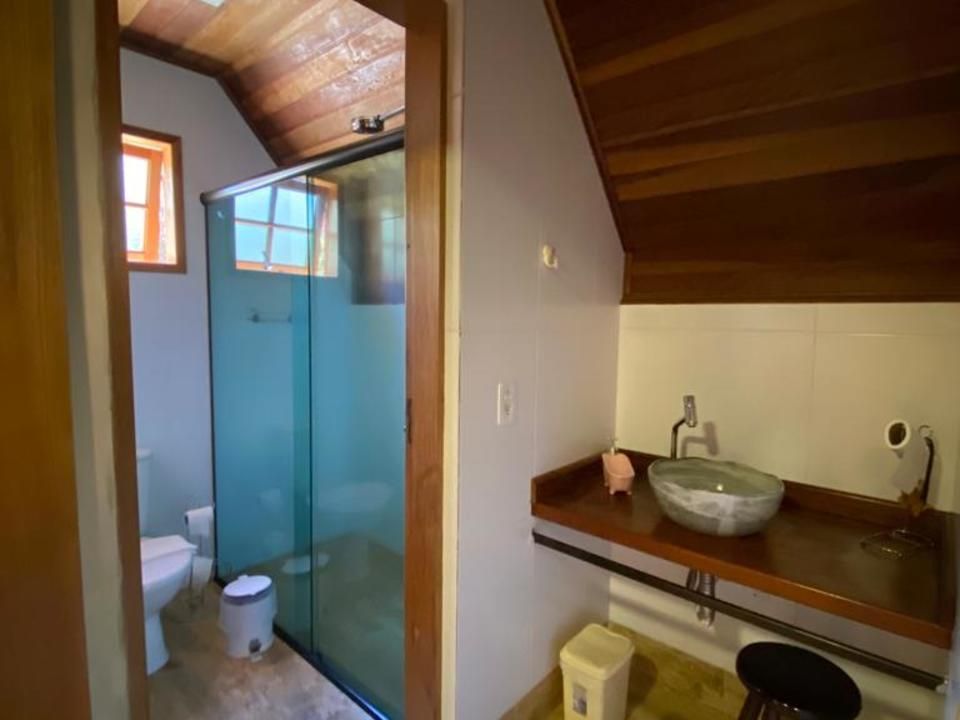 Banheiro com box de vidro, pia com bancada de pedra e vaso sanitário. Detalhes em madeira e iluminação natural.