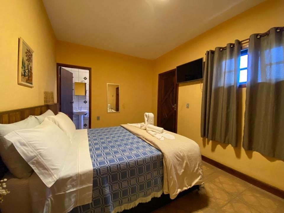 Quarto com cama, colcha azul estampada, paredes amarelas, porta do banheiro aberta.
