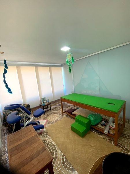 Sala de massagem com maca, cadeira e acessórios. Tons de verde e bege.