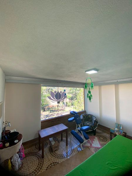 Sala de massagem com maca, cadeira e janela decorada com uma flor de lótus.