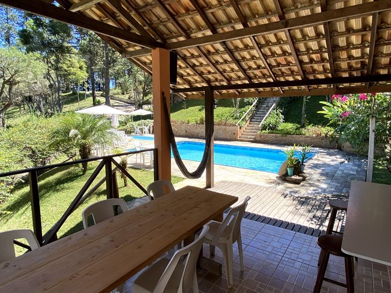 Varanda coberta com mesa e cadeiras de madeira com vista para a piscina e o jardim.