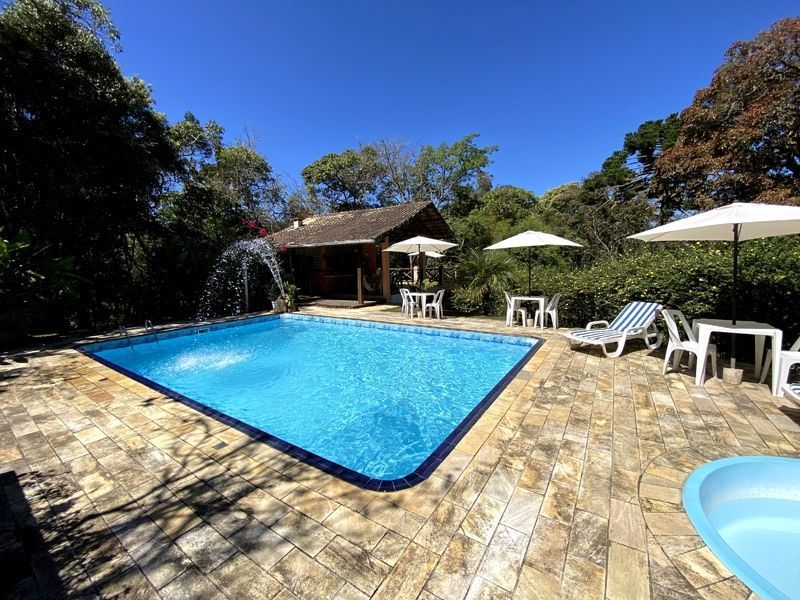 Piscina com fonte, mesas, guarda-sóis e pequena construção em um ambiente ensolarado ao ar livre.