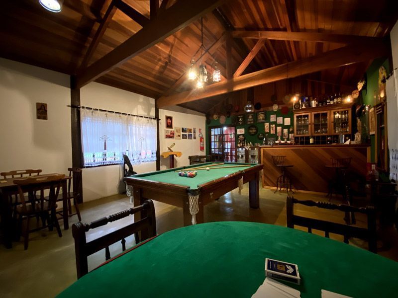 Salão de bilhar com mesa de bilhar, bar, teto de madeira e mesa de pôquer verde.