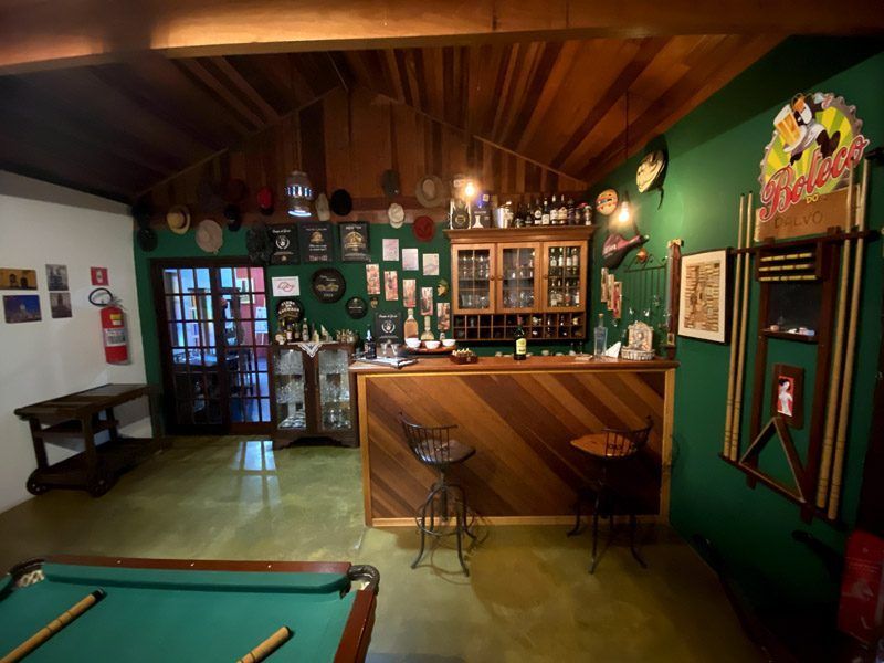 Interior de um bar com mesa de bilhar, balcão de madeira, paredes verdes e decoração variada.