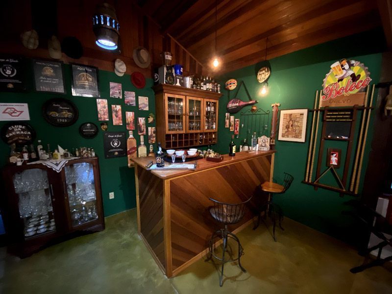 Bar aconchegante em casa com balcão de madeira, paredes verdes, garrafas de bebidas alcoólicas e decoração vintage.