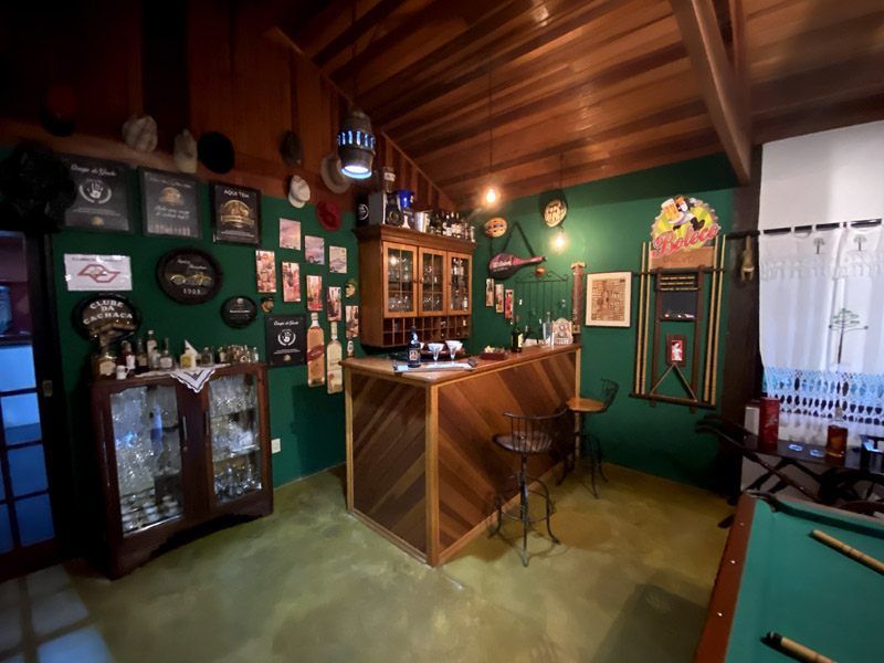 Aconchegante sala de bar com painéis de madeira e paredes verdes, equipada com bar, armário de bebidas e mesa de bilhar.