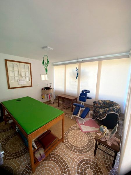 Sala de massagem terapêutica com mesa verde, cadeira azul e piso estampado.