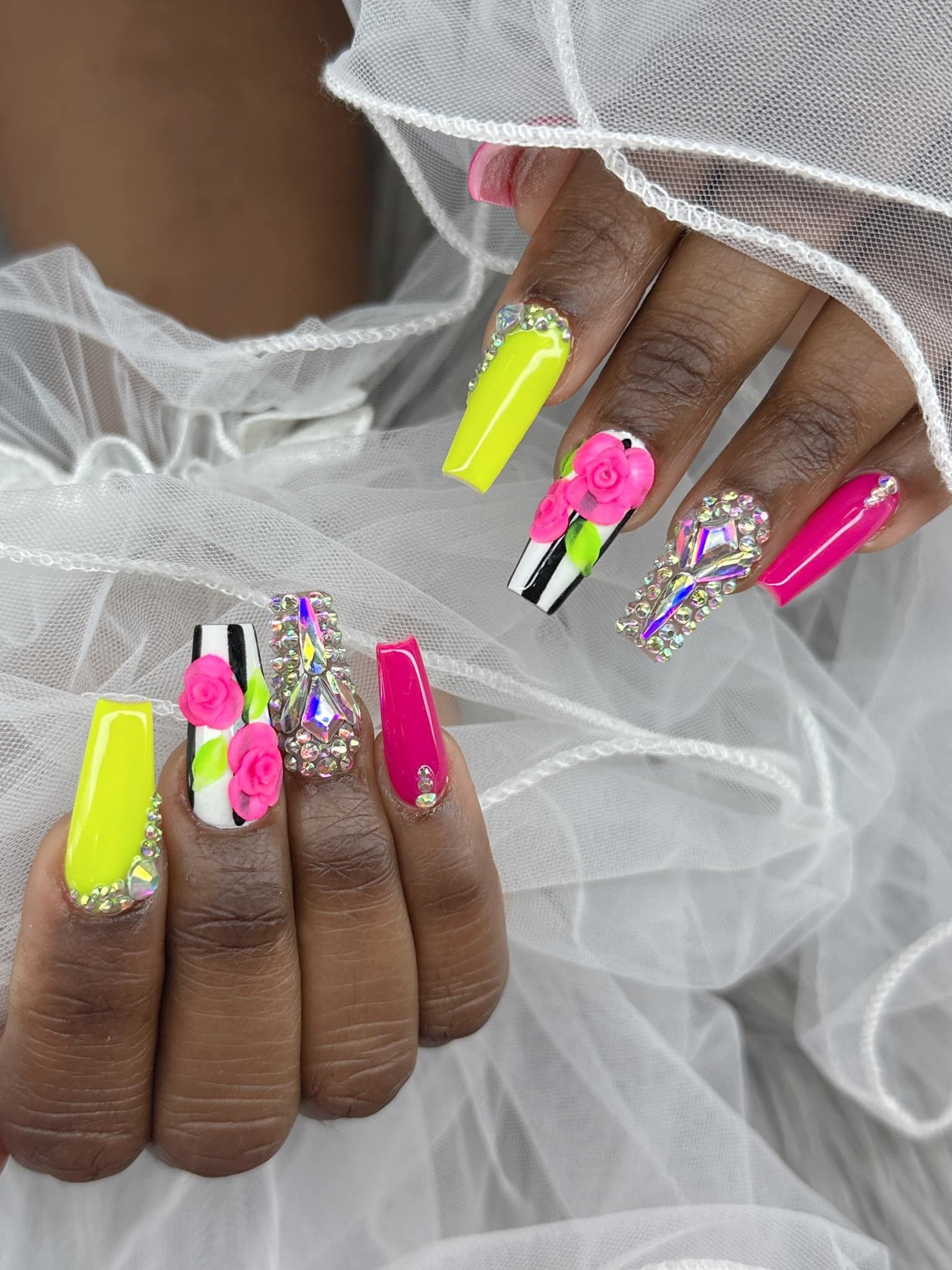 Long coffin-shaped nails with neon yellow, hot pink, black-and-white stripes, 3D floral accents, and rhinestone detailing.