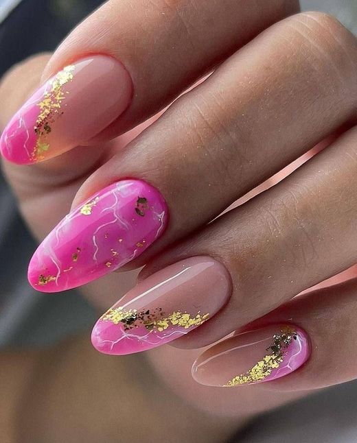 A hand showing oval-shaped nails with pink marble designs, translucent pink polish, and gold leaf accents.