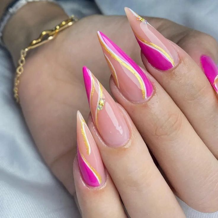 Stiletto nails with a nude base, vibrant magenta tips, and elegant gold swirl accents.