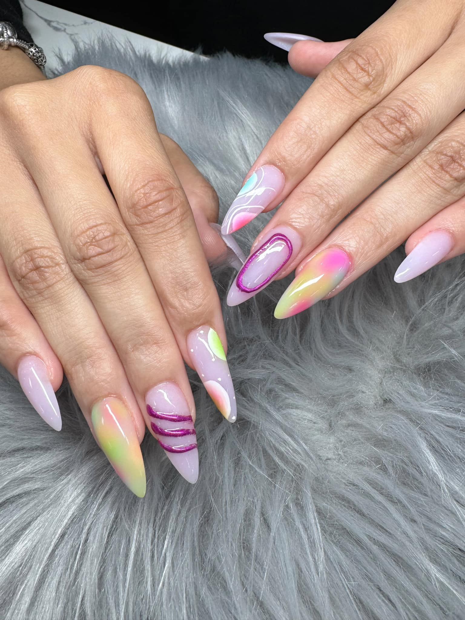 Close-up of hands with long, almond-shaped nails featuring a mix of ombre, abstract art, and textured magenta swirls.