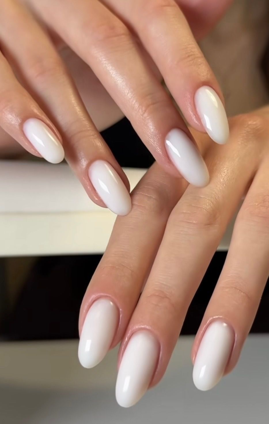 Two hands with long white ombré manicured nails overlapping on a soft background