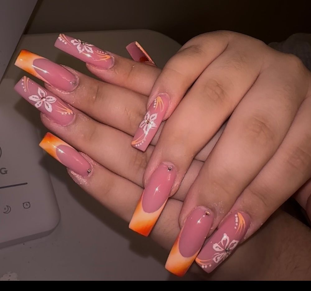 Hands with pink and orange ombré acrylic nails and white floral nail art resting on a surface