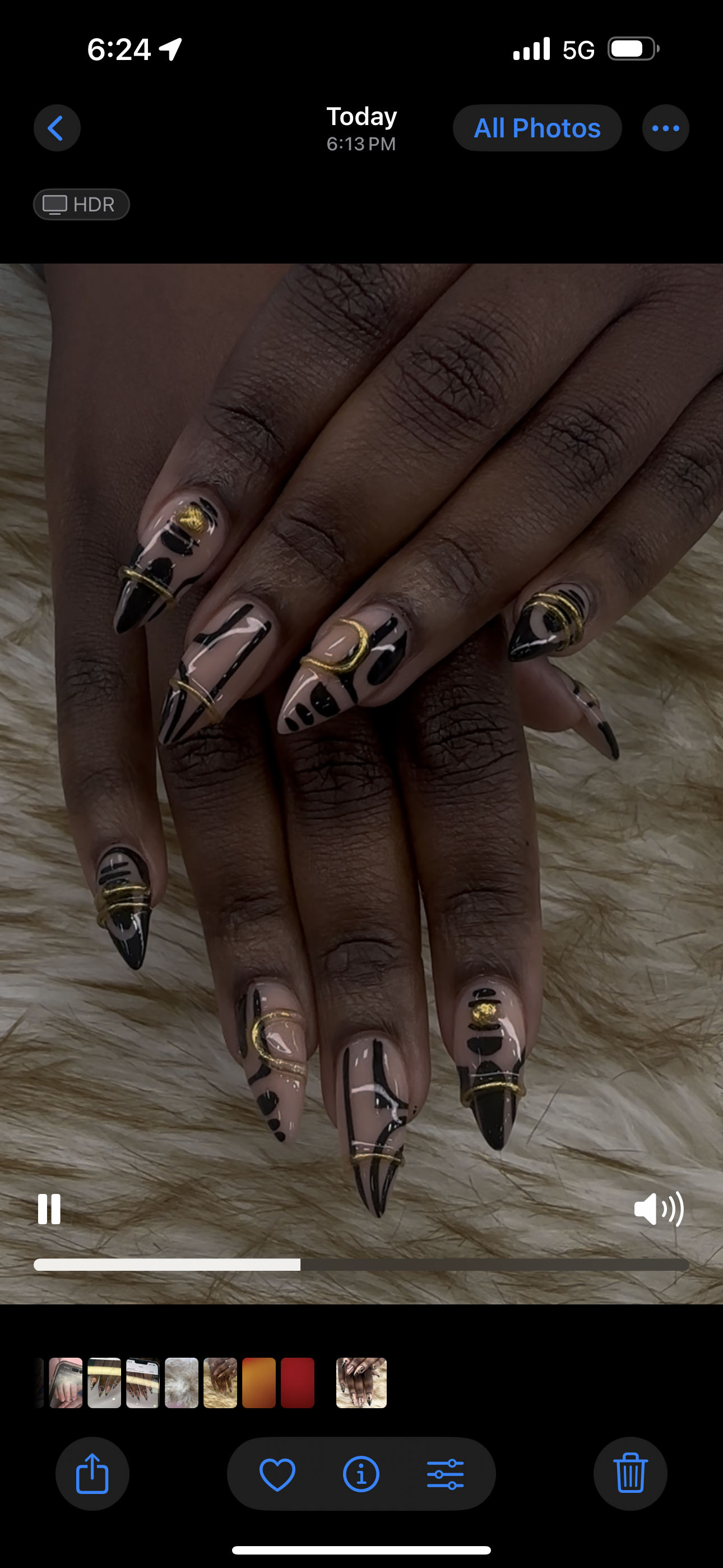 Hands with long brown-and-gold patterned acrylic nails crossed on a soft fur surface.