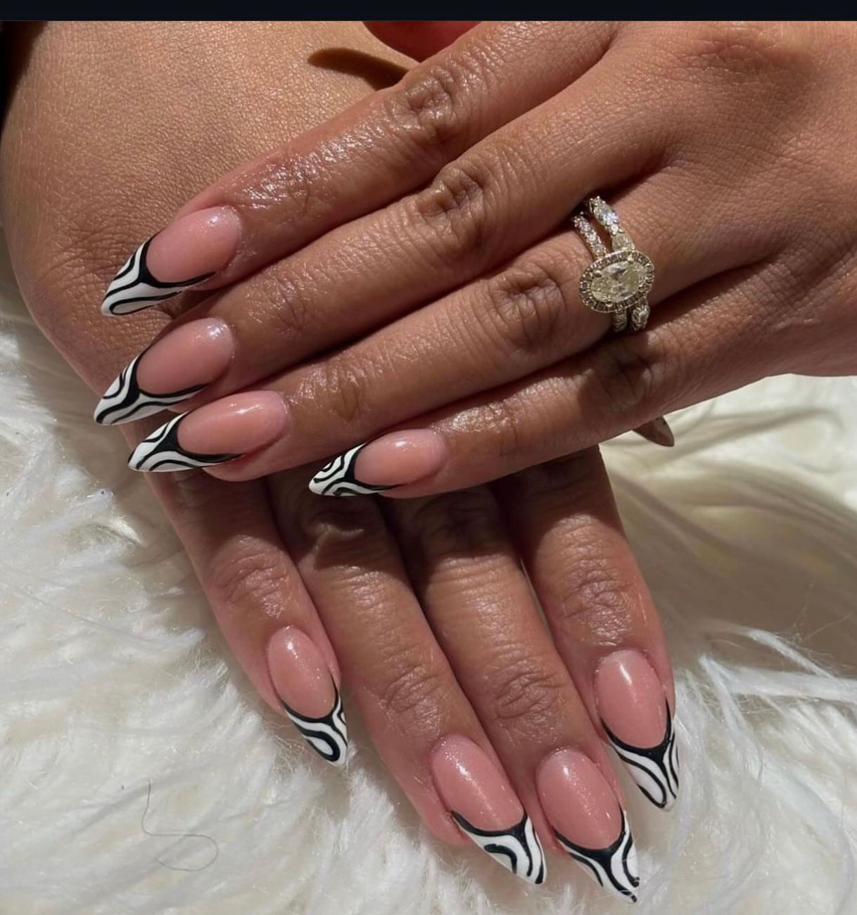 Close-up of hands with pink and white stiletto nails and a diamond ring on a fluffy white background