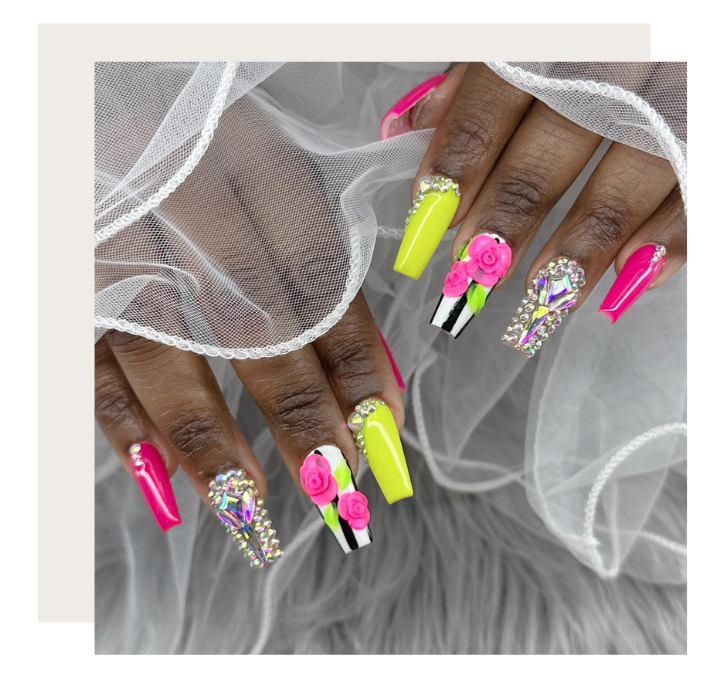 Manicured hands with long, neon pink and lime green coffin-shaped nails featuring 3D floral accents and crystal gems.