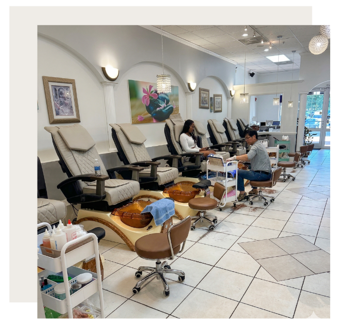 Interior view of a nail salon with rows of beige pedicure chairs and rolling workstations on a white tiled floor.