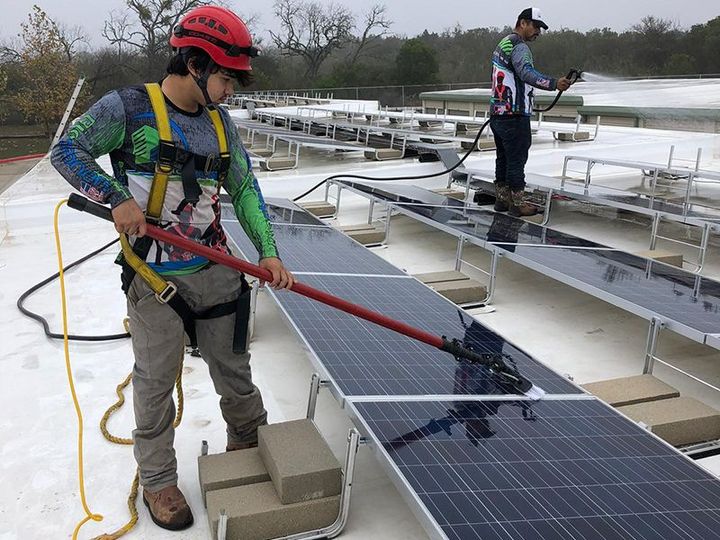 Two men are cleaning solar panels on a roof.