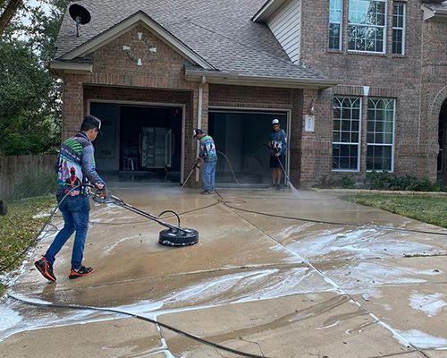 A man is using a pressure washer to clean a driveway in front of a house.