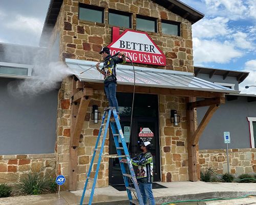 A man is standing on a ladder cleaning the front of a building.