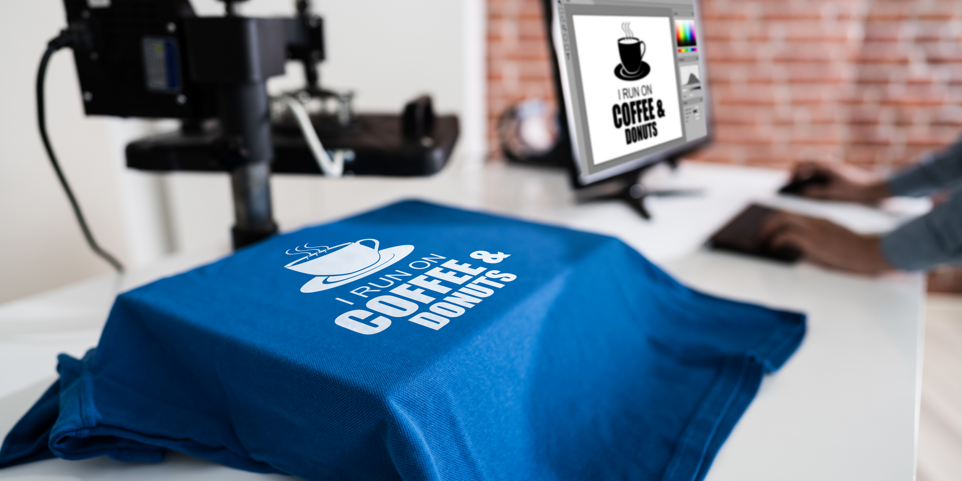 A blue t-shirt with a printed design, heat press, and computer screen showing the design.