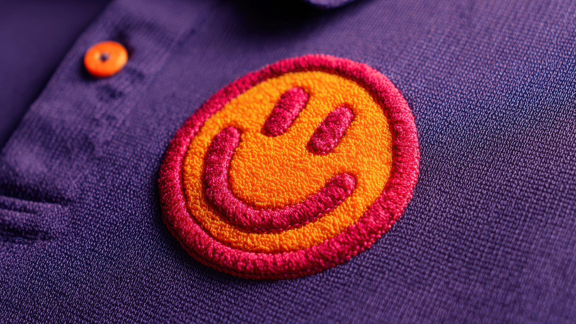 Purple shirt with orange smiley face patch and button.