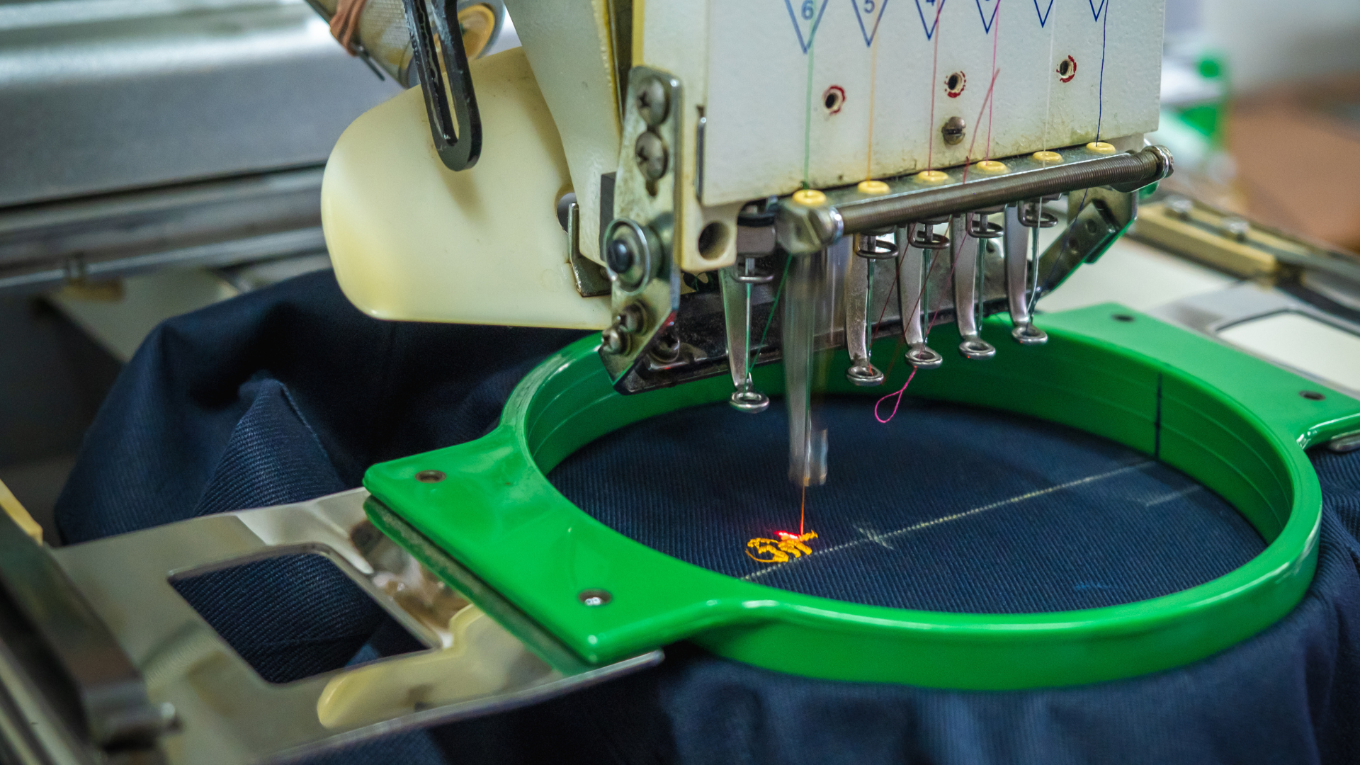 Embroidery machine stitching colorful design onto dark blue fabric held in a green hoop.