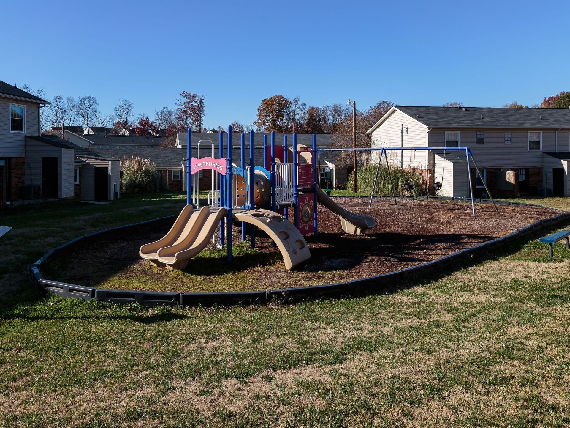 Colorful playground with slides and climbing structure in a grassy neighborhood park