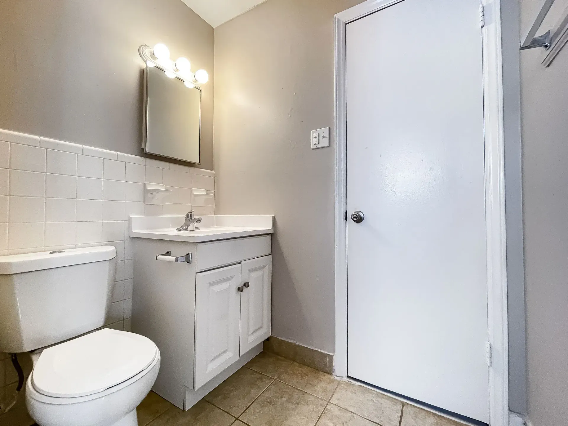 Small bathroom with toilet, vanity sink, mirror, white door, and tiled wall
