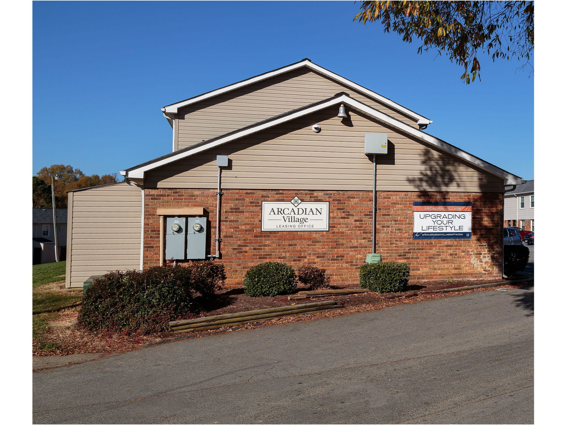 Small brick building with tan siding and signs, viewed from a parking lot under a blue sky