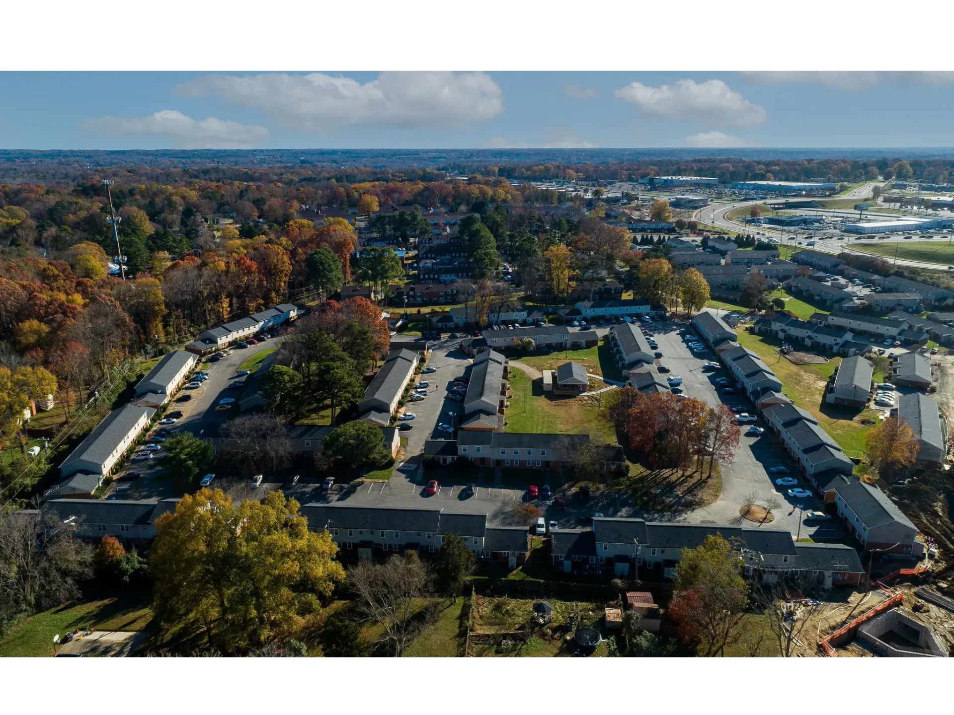 Aerial view of a suburban apartment complex surrounded by autumn trees and roads under a blue sky