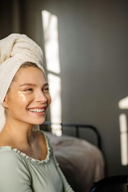 Smiling person with towel wrapped around head sitting in a softly lit bedroom