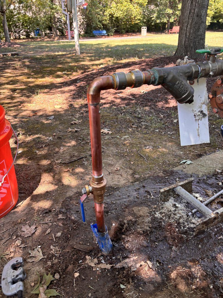 Water pipes, copper and brass, emerging from the ground with valves, in a park setting.