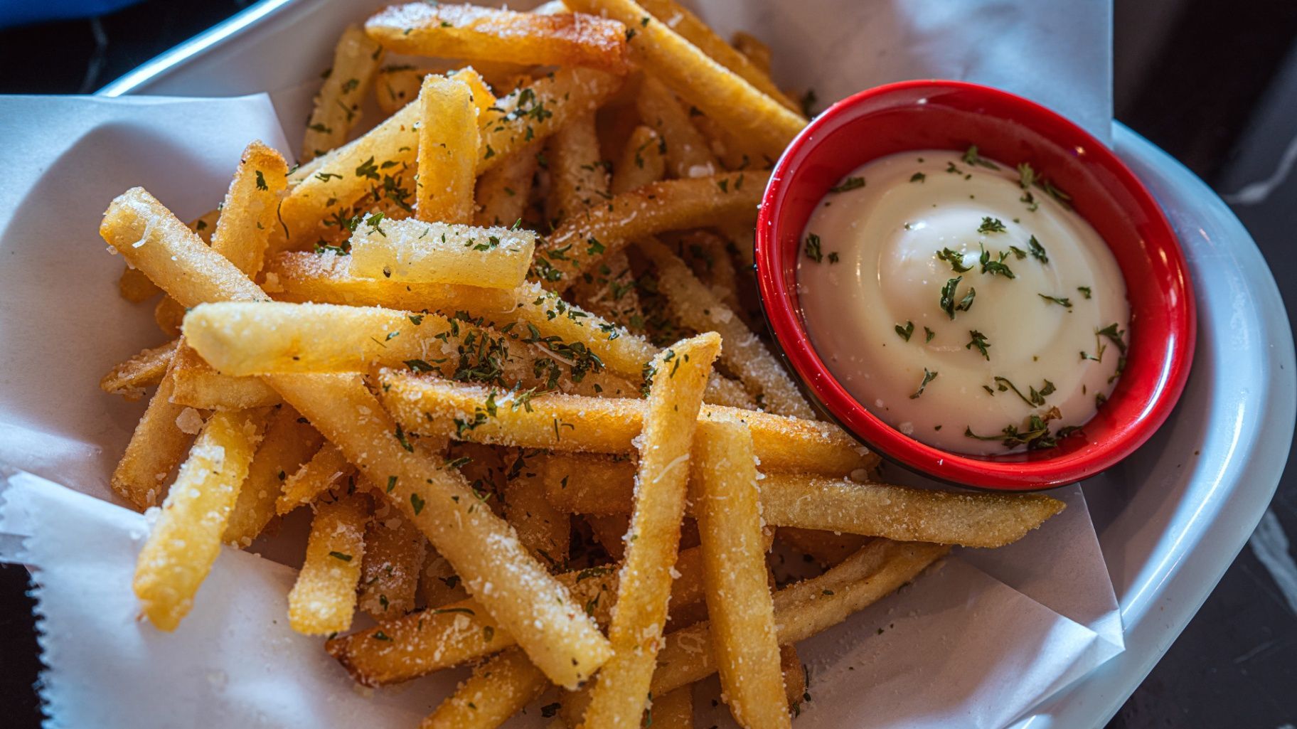 Basket of seasoned French fries with a side of creamy dipping sauce in a red ramekin.