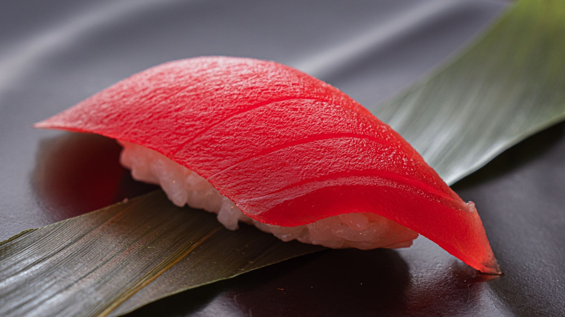 Red sushi nigiri on a dark leaf-lined plate