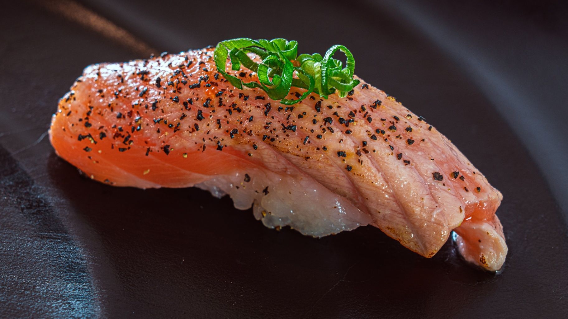Salmon nigiri sushi topped with green onions on a dark plate