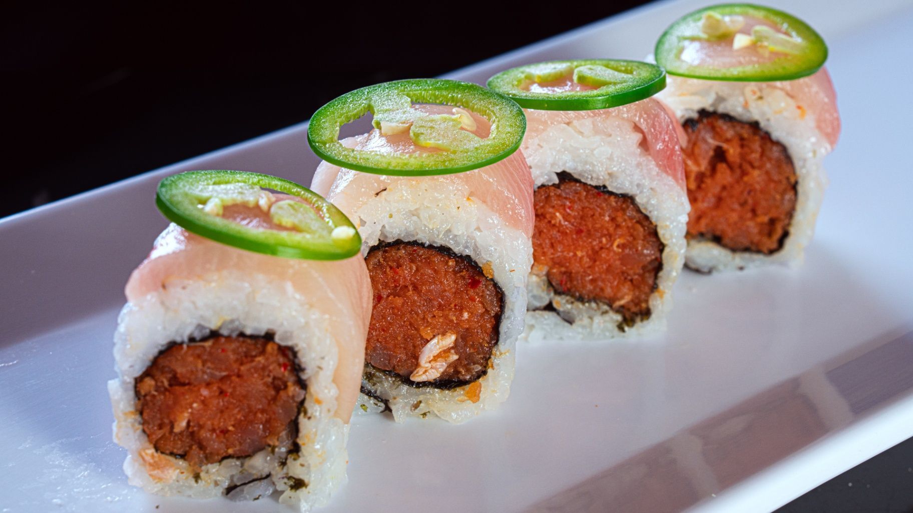 Sushi rolls topped with jalapeño slices on a white rectangular plate