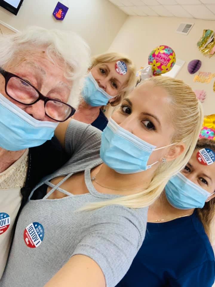 Four people in face masks, smiling, taking a selfie. Each has a 