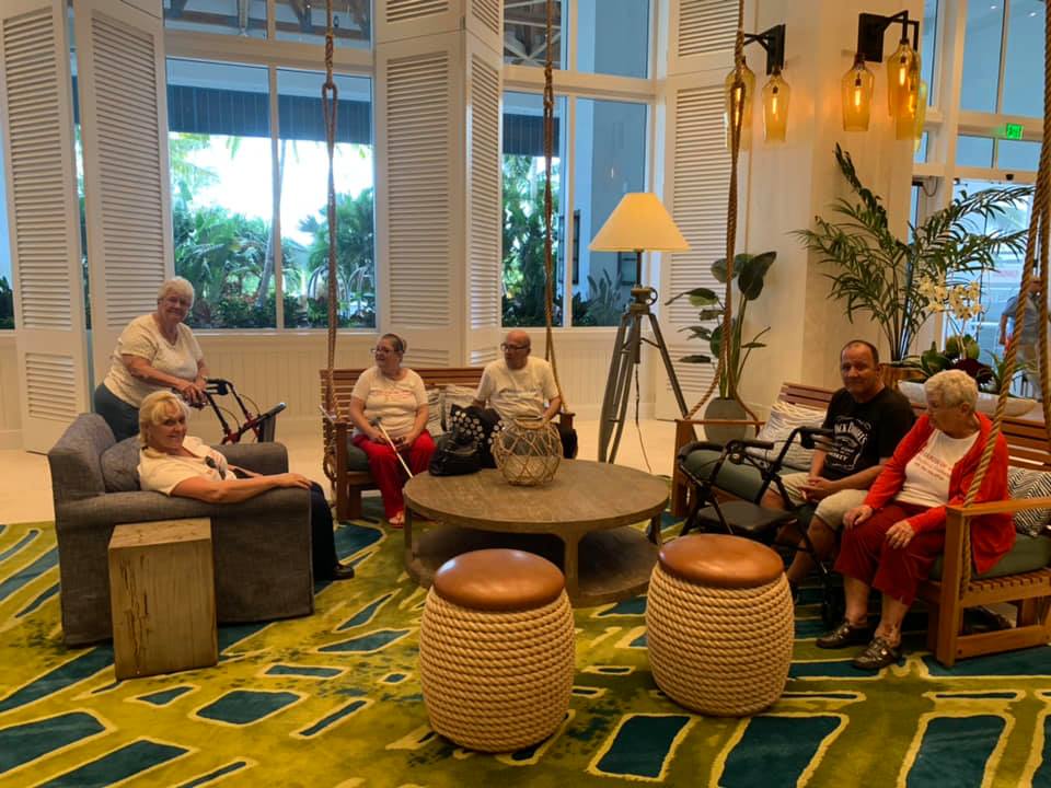 People seated in a well-lit hotel lounge with swing seating, plants, and a patterned rug.