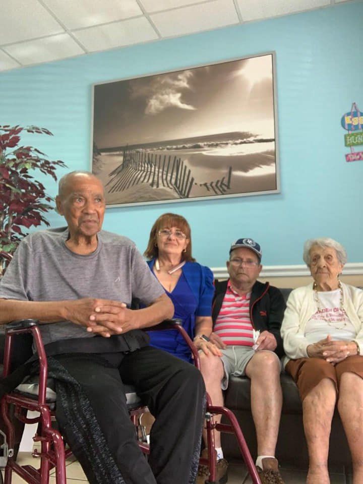 Four people seated on a couch indoors; one in a wheelchair. Blue wall with beach scene art.