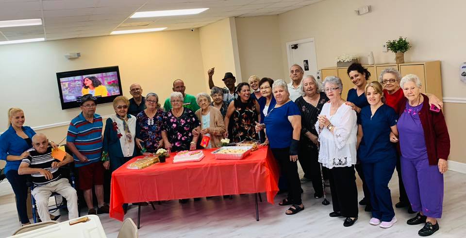 Group of people at a celebration, standing around tables with a cake.