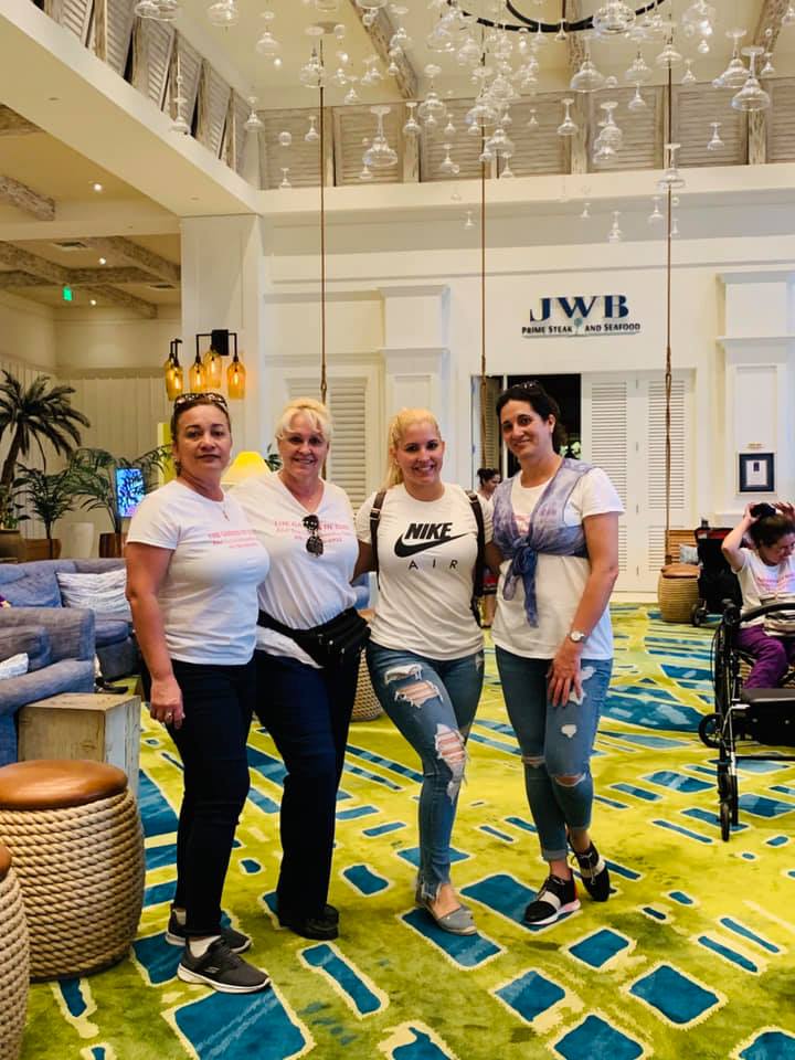 Four people pose in a hotel lobby with a large green and blue carpet. One has a Nike shirt, and the others wear white tops