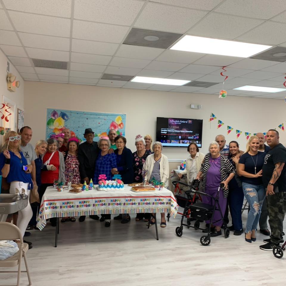 Group of people at a birthday celebration with a table, cake, and decorations.
