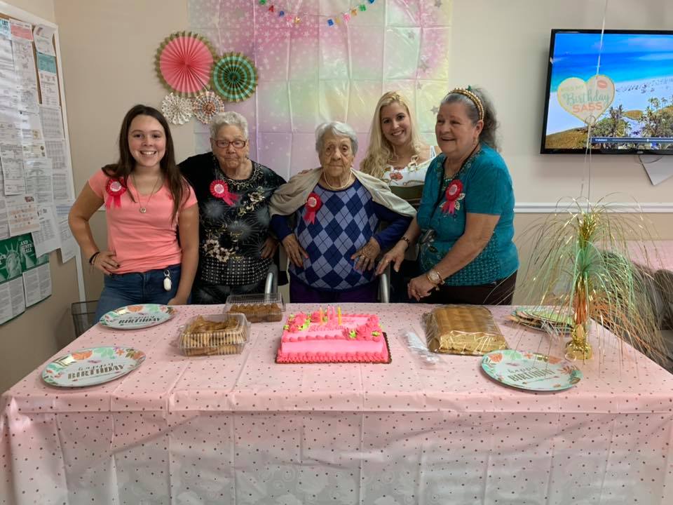 Group of people celebrating a birthday, pink decorations, cake on a table.
