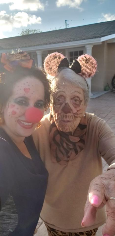 Two people in costume. One has red nose, other has mouse ears and face paint. Outdoors, pointing.