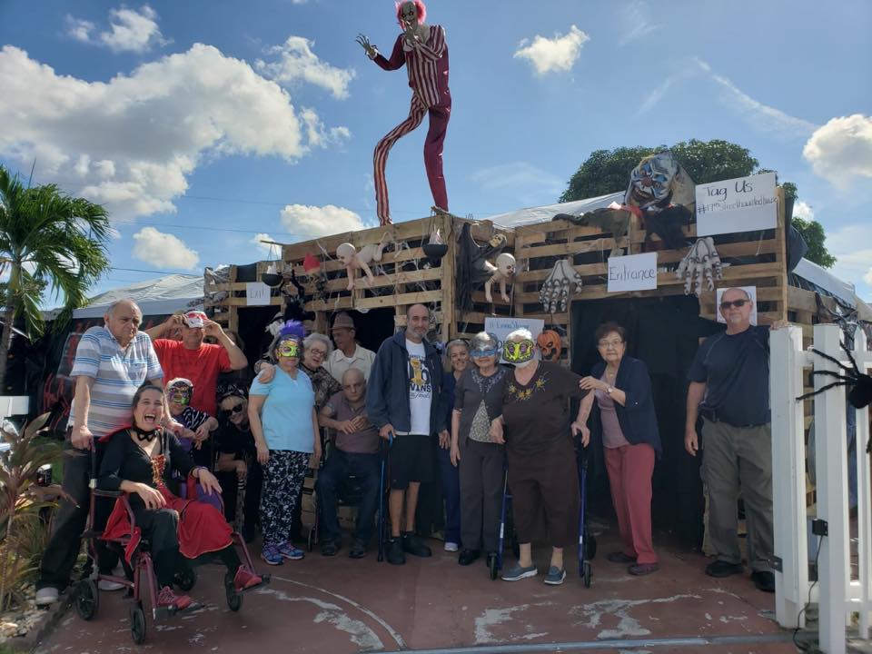 Group of people pose with Halloween decorations outside. A tall skeleton figure stands atop the structure.