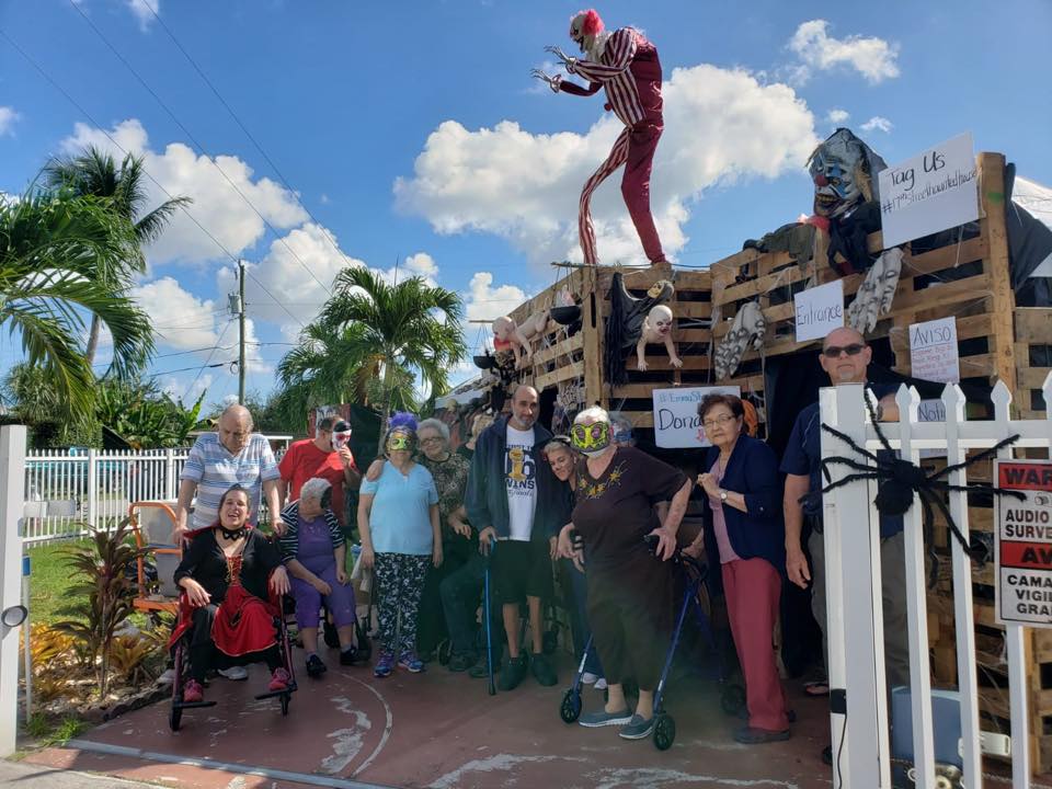 Group of people in costumes posing in front of a Halloween-themed display with a skeleton figure.